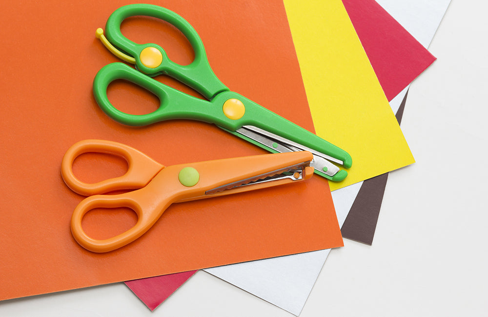 Eine Kinderschere in Orange und Grün liegen auf Bastelpapier.