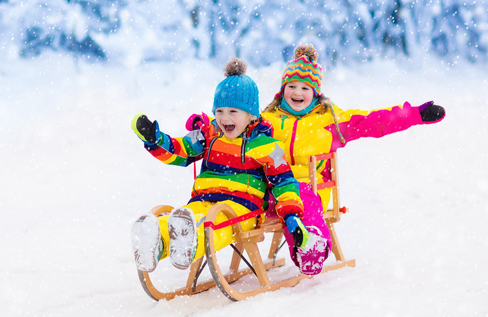 Kinder fahren auf einem Schlitten im Schnee einen Berg herunter.