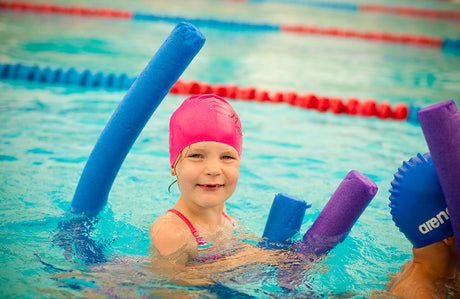 Ein Kind schwimmt mit einer Schwimmnudel im Schwimmunterricht.