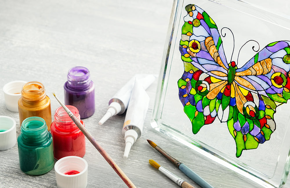 Mit Glasmalfarben und Pinsel ein Schmetterling auf einer Glasscheibe gemalt.